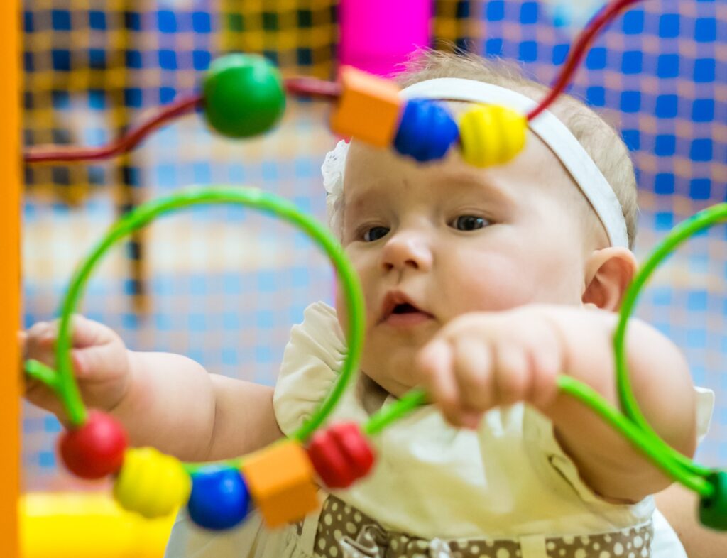 An infant girl playing with a bead maze toy at an infant daycare